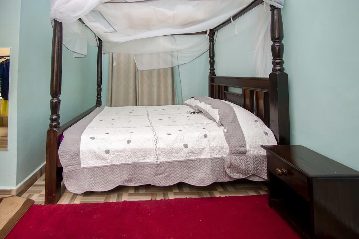 A four-poster bed with a canopy, a wooden nightstand, and a red carpet.