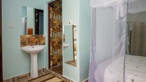 Un baño con lavamanos, espejo y puerta que da a la zona de la ducha.