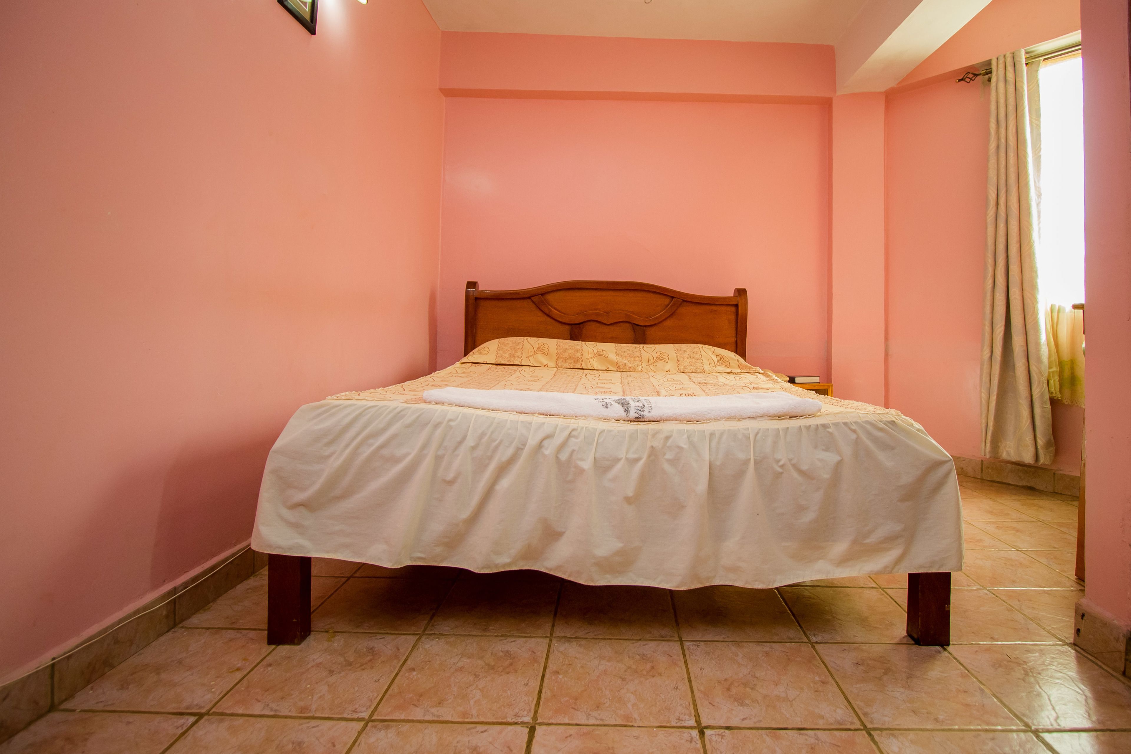 Ein Einzelbett mit Holz-Kopfteil in einem Zimmer mit rosafarbenen Wänden und Fliesenboden.