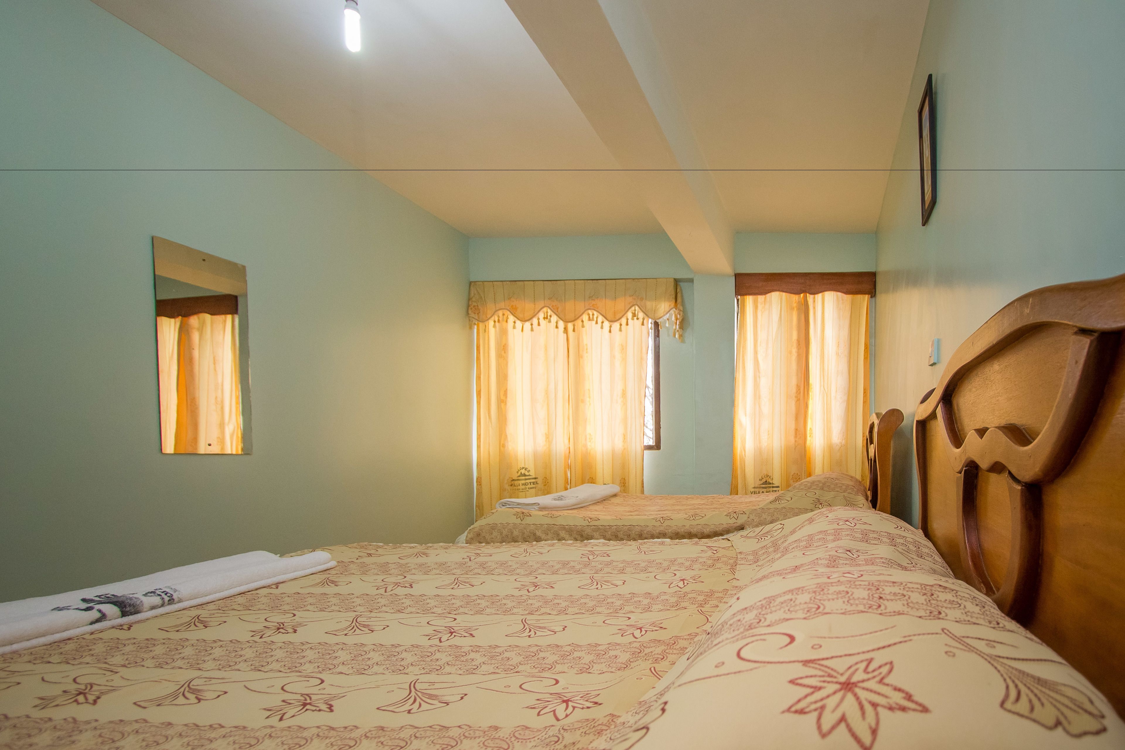Habitación de hotel con dos camas, cabecero de madera, espejo y ventana con cortinas.