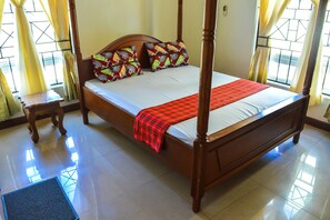 A four-poster bed with a red plaid bedspread, two decorative pillows, and a wooden nightstand.