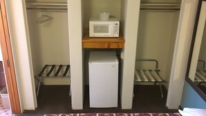 Ein kompakter Raum mit einem weißen Kühlschrank, einer Mikrowelle auf einem Holzregal und einem Metallgestell.