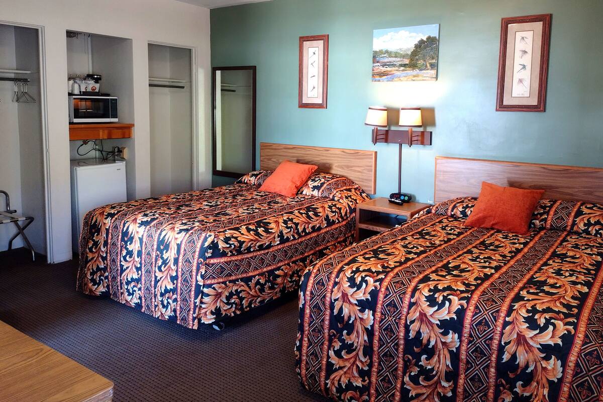 A hotel room with two beds, a desk, a lamp, and a painting on the wall.