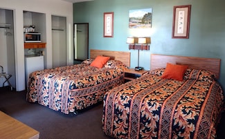 Una habitación de hotel con dos camas, un escritorio, una lámpara y un cuadro en la pared.