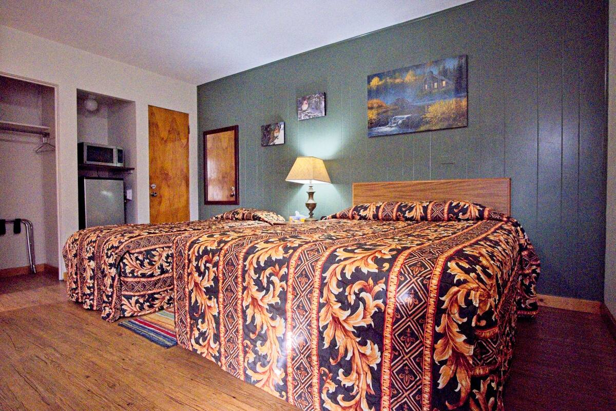 A hotel room with a large bed, a wooden headboard, a small table with a lamp, and a painting on the wall.