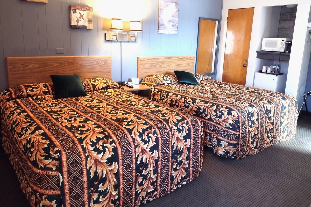 A hotel room with two beds, a desk, a microwave, and a small cabinet.