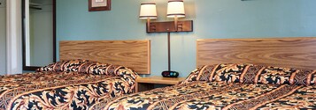 Habitación de hotel con dos camas, cada una con ropa de cama estampada, una mesita de noche con un reloj y dos lámparas fijadas a la pared.