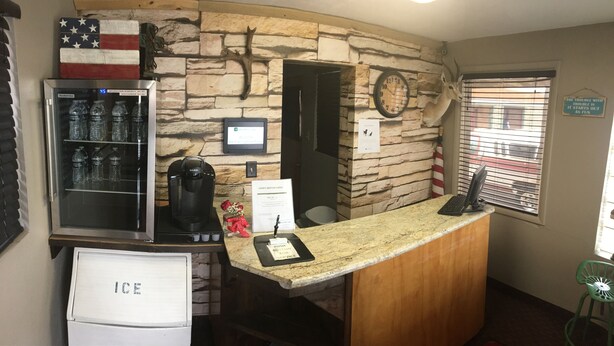 Ein Empfangsbereich mit Steinwand, einem mit 'ICE' beschrifteten Kühlschrank, einem Wasserspender, einer Kaffeemaschine und einem Schild für 'Sieney Motor Lodge'.