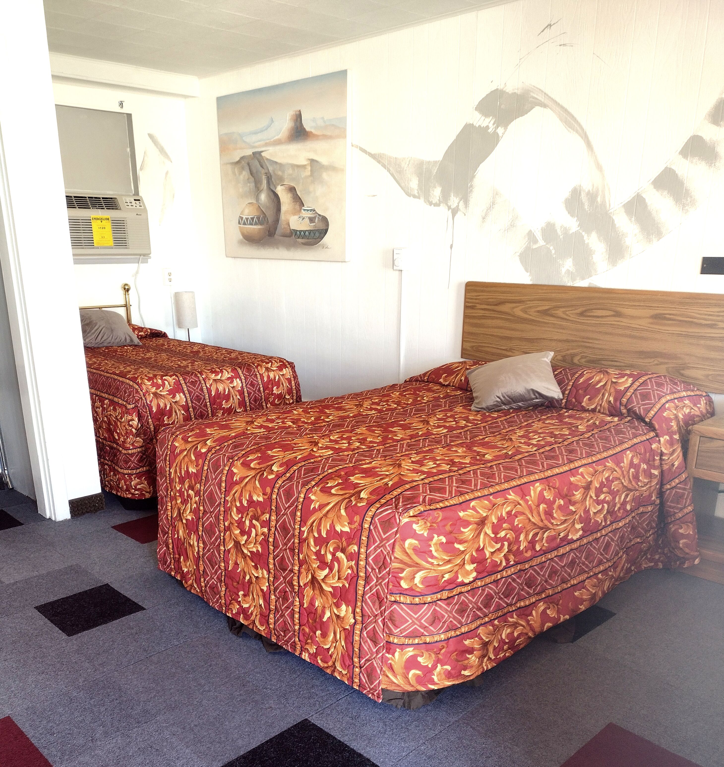 A hotel room with two beds, a wooden headboard, a painting on the wall, and a radiator.