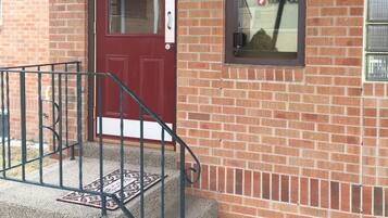 A brick building with a red door, a small window with an 'OPEN' sign, and a number '2031' on the wall.
