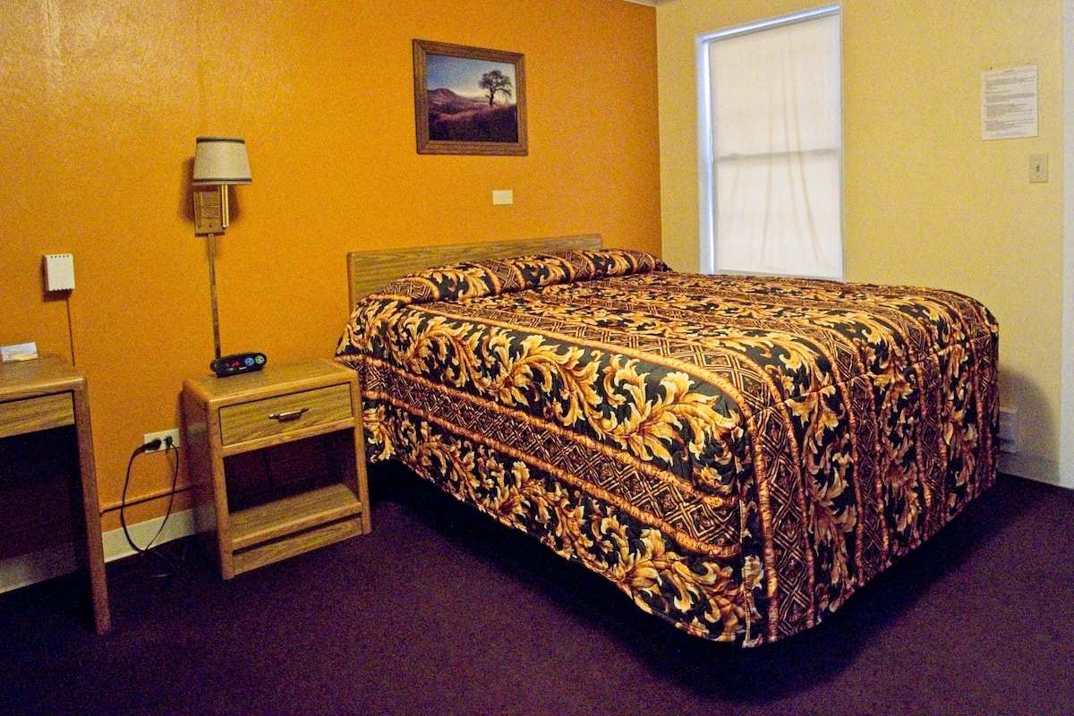 A hotel room with a bed, a desk, a lamp, and a picture on the wall.