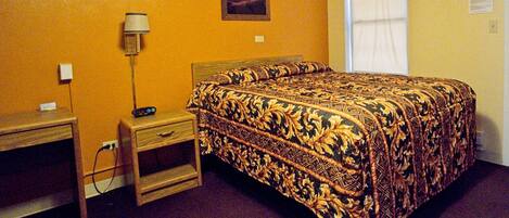 Una habitación de hotel con cama, escritorio, lámpara y un cuadro en la pared.