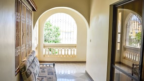 A corridor with a bench, a window with decorative metal bars, and a view of greenery outside. - Platinum Hotel (Mombasa)