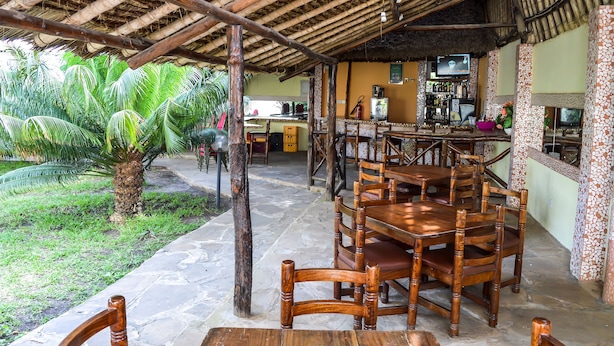 An outdoor dining area with wooden tables and chairs, a thatched roof, and a bar area with a television. - Platinum Hotel (Mombasa)