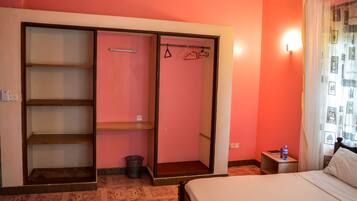 Hotelkamer met een bed, een garderobe met planken, een klein tafeltje met een waterfles en een wandlamp.