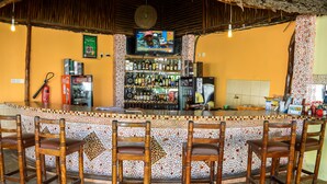 A bar area with a tiled counter, wooden chairs, a television screen, and a variety of bottles and glasses. - Platinum Hotel (Mombasa)