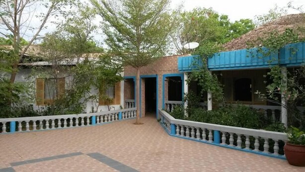 A courtyard with a tiled floor, a blue and white building with a thatched roof, and a potted plant.