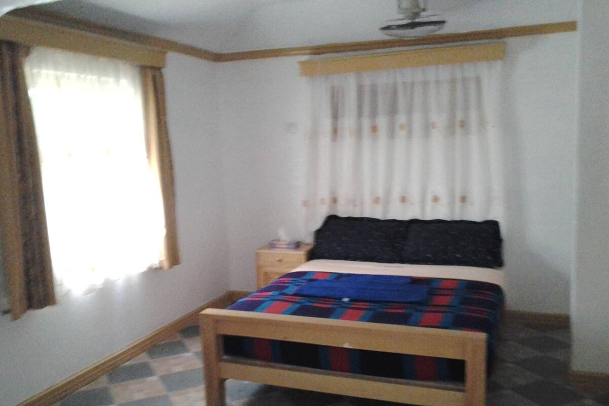 A bedroom with a bed, a nightstand, a window with curtains, and a checkered floor.