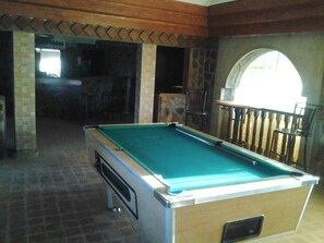 A pool table in a room with stone walls and a wooden ceiling.