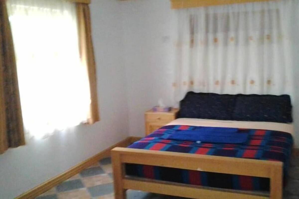 A bedroom with a bed, a nightstand, a window with curtains, and a checkered floor.