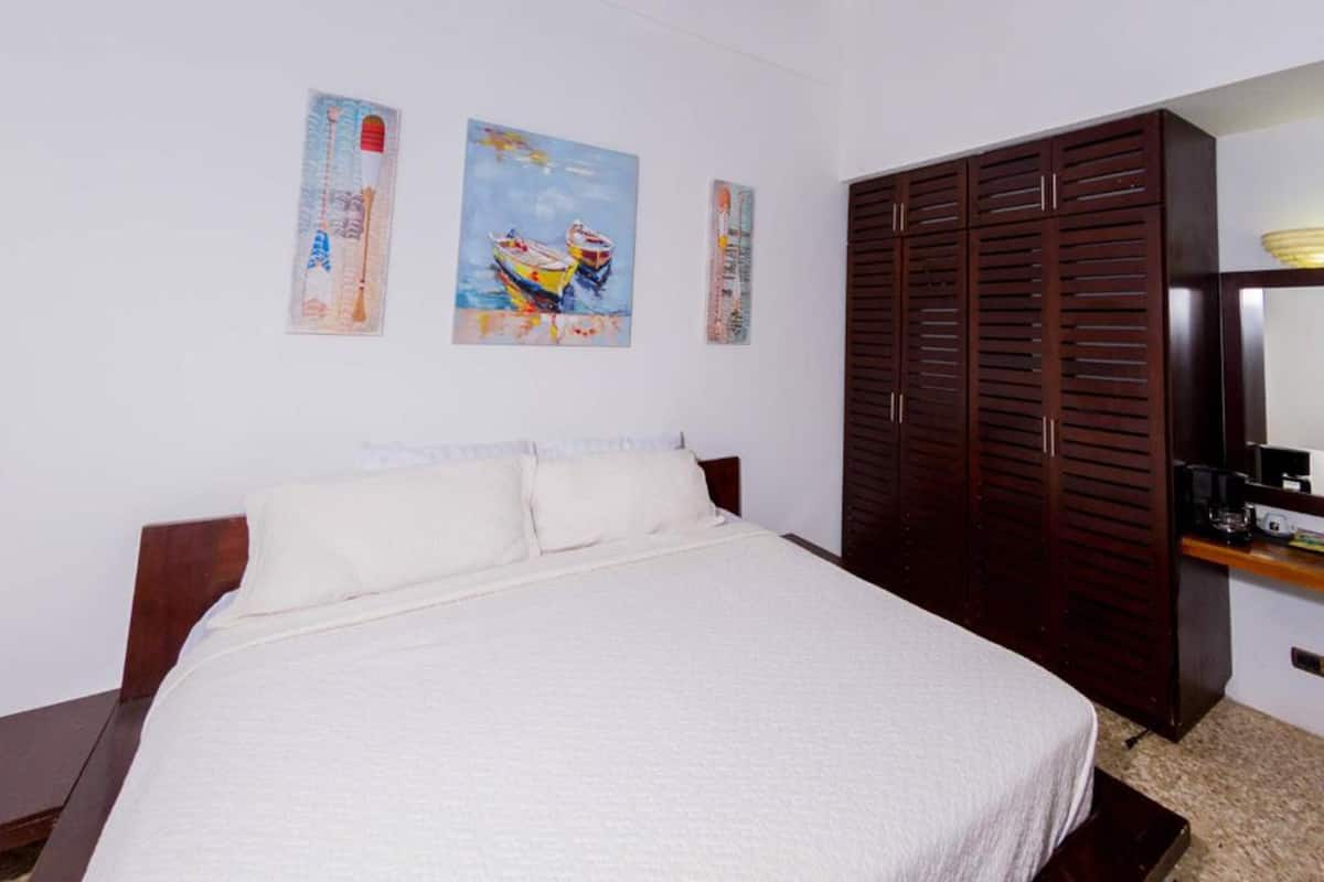 Quarto com cama, guarda-roupa de madeira e duas pinturas penduradas na parede.
