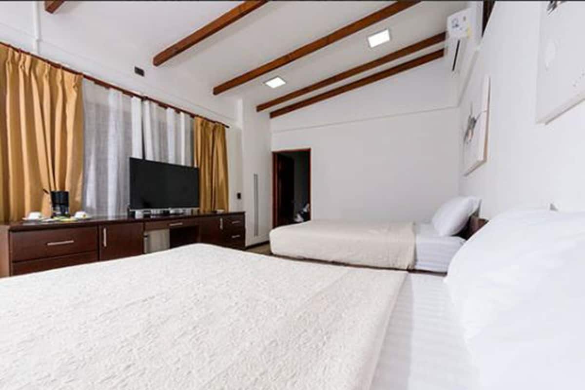 Quarto de hotel com uma cama grande, uma cama menor, uma escrivaninha com televisão e vigas de madeira no teto.