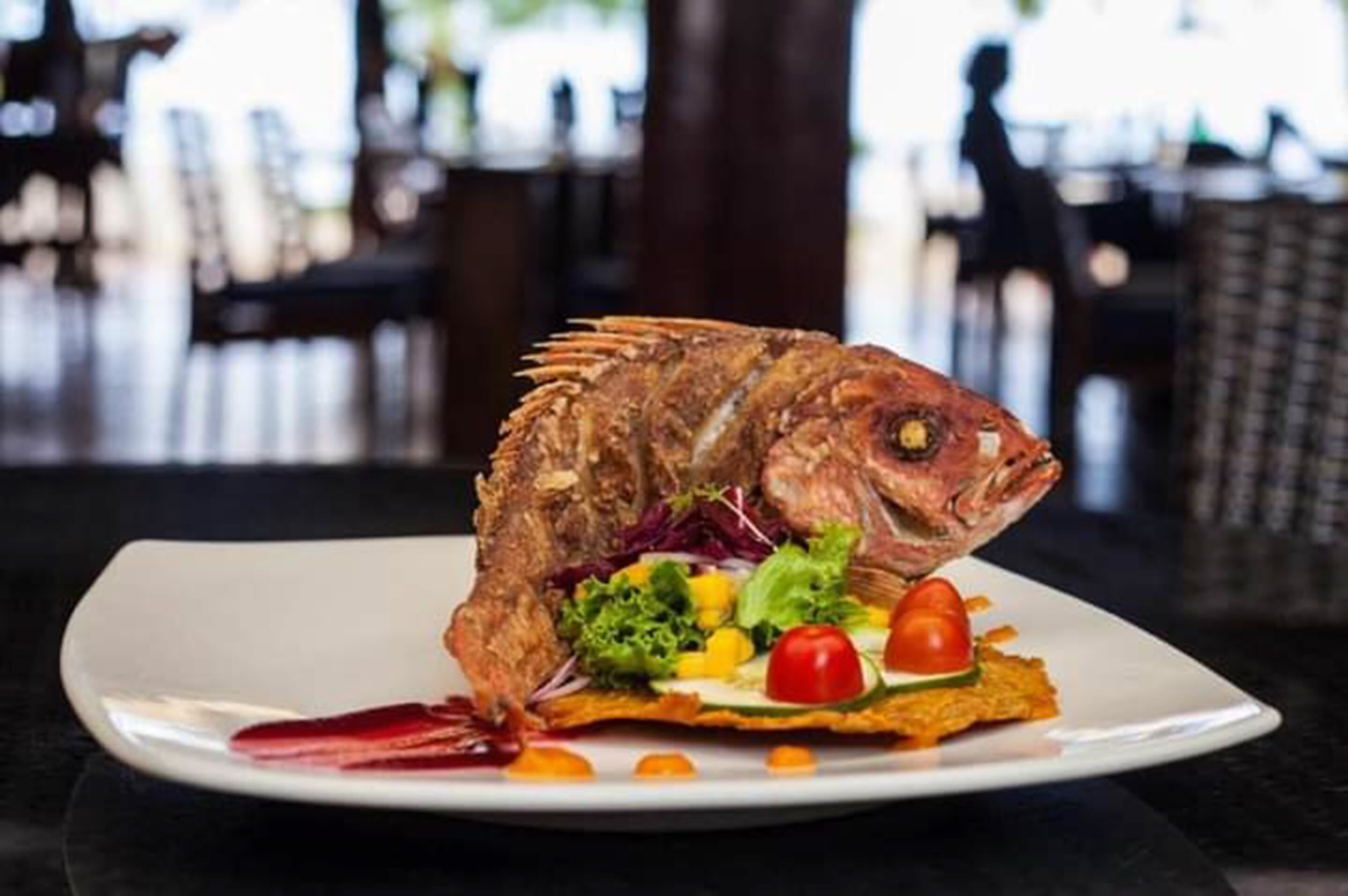 A plate with a whole cooked fish, salad, and vegetables.