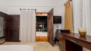Une chambre d’hôtel comprenant un lit, un bureau avec des tiroirs, une télévision et une vue sur un espace extérieur avec une piscine et de la verdure.