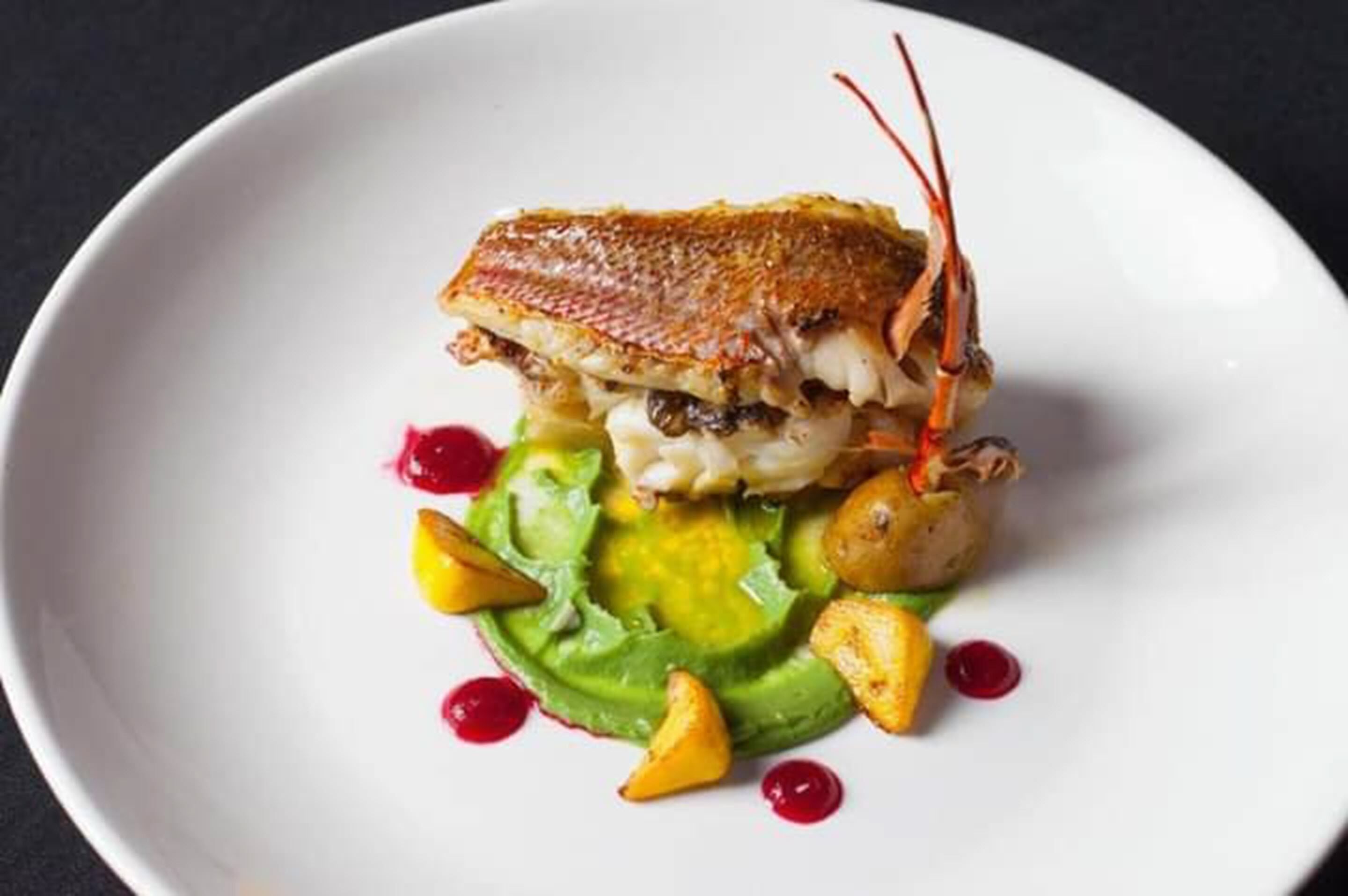 Un plato con pescado asado, aguacate y patatas al horno.