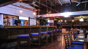 Un restaurant avec des tables et des chaises en bois, un coin bar et des luminaires suspendus.