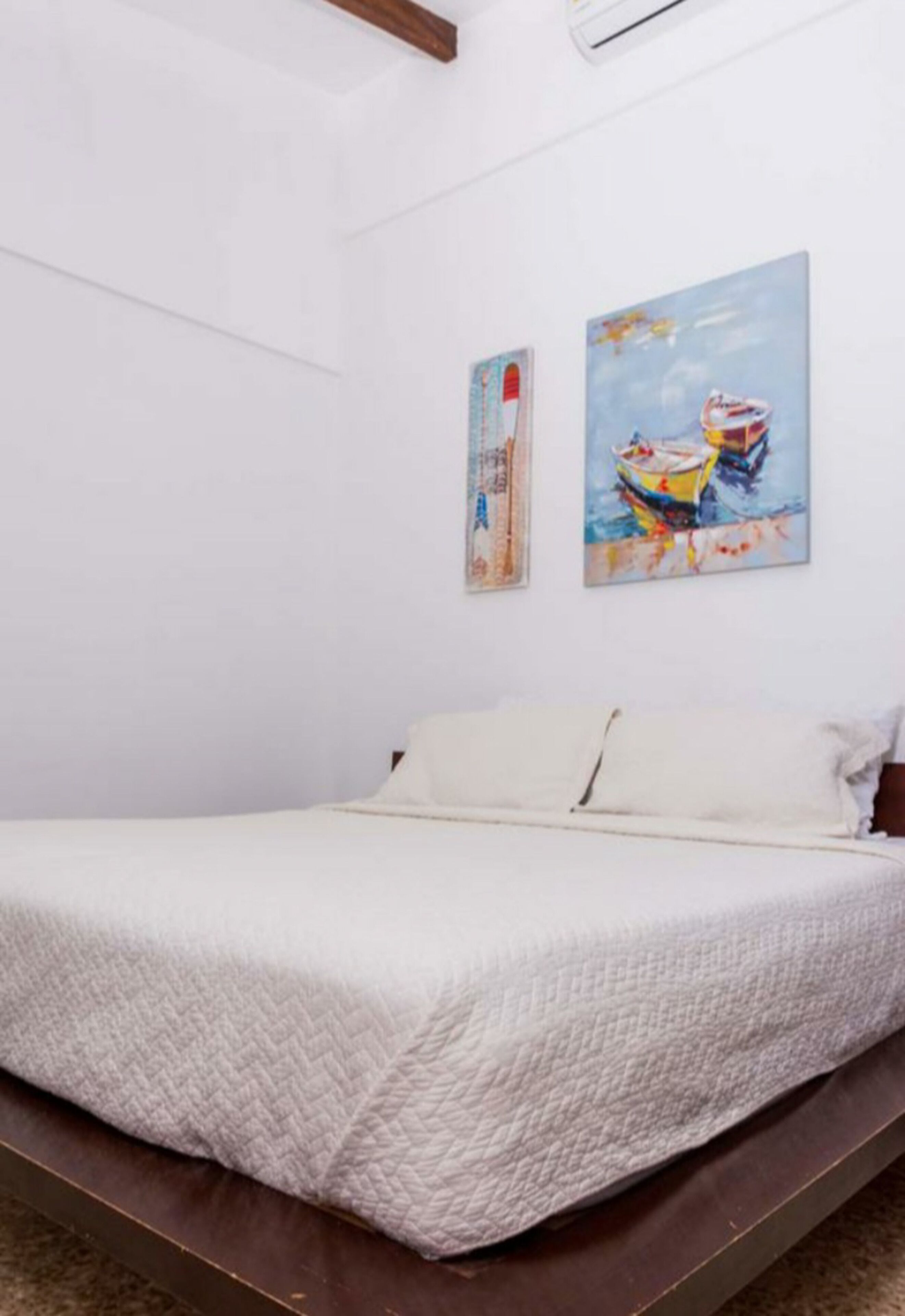 A bedroom with a bed, white walls, and two paintings.