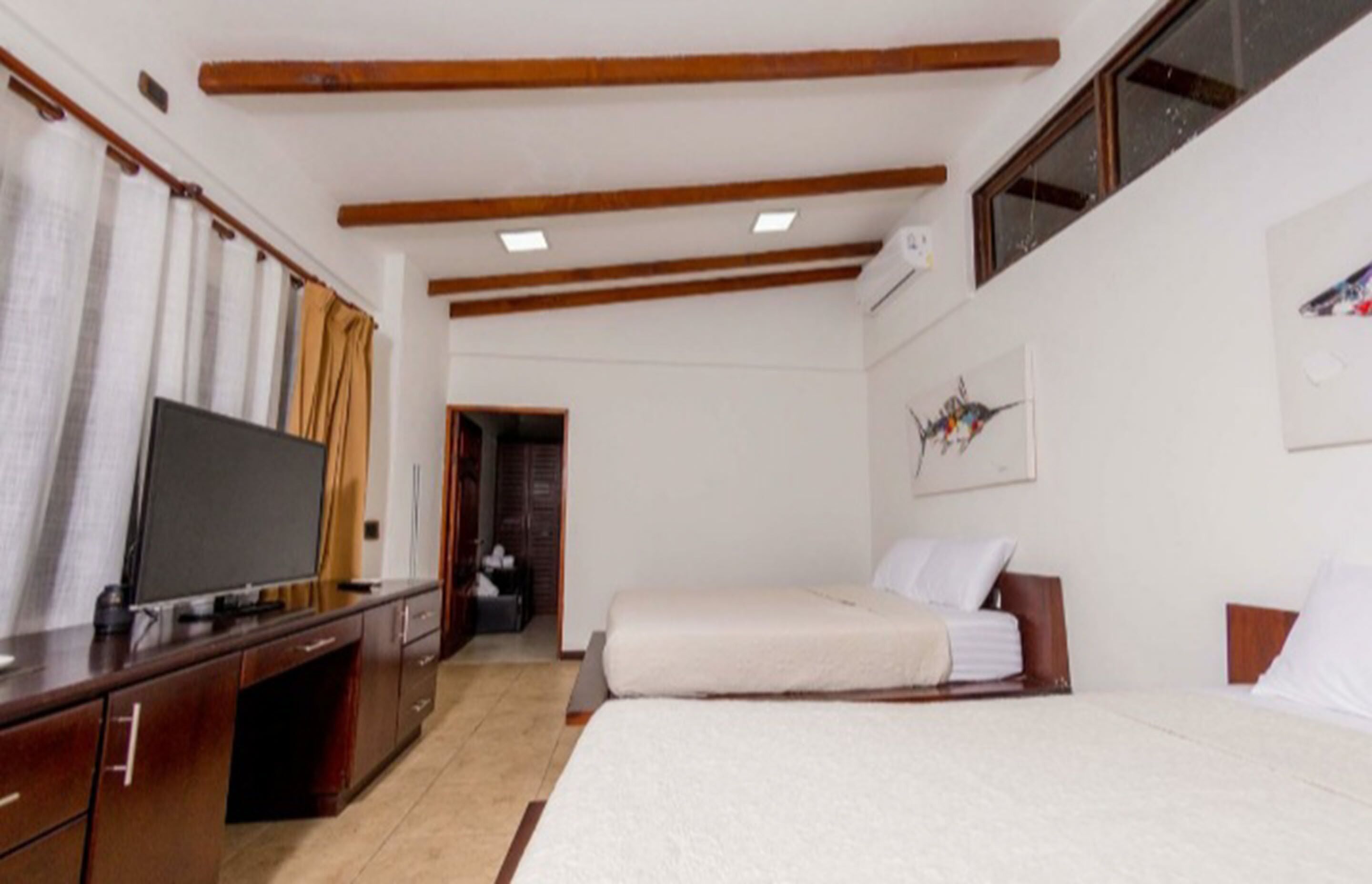 A hotel room with two beds, a TV, wooden beams on the ceiling, and a painting on the wall.