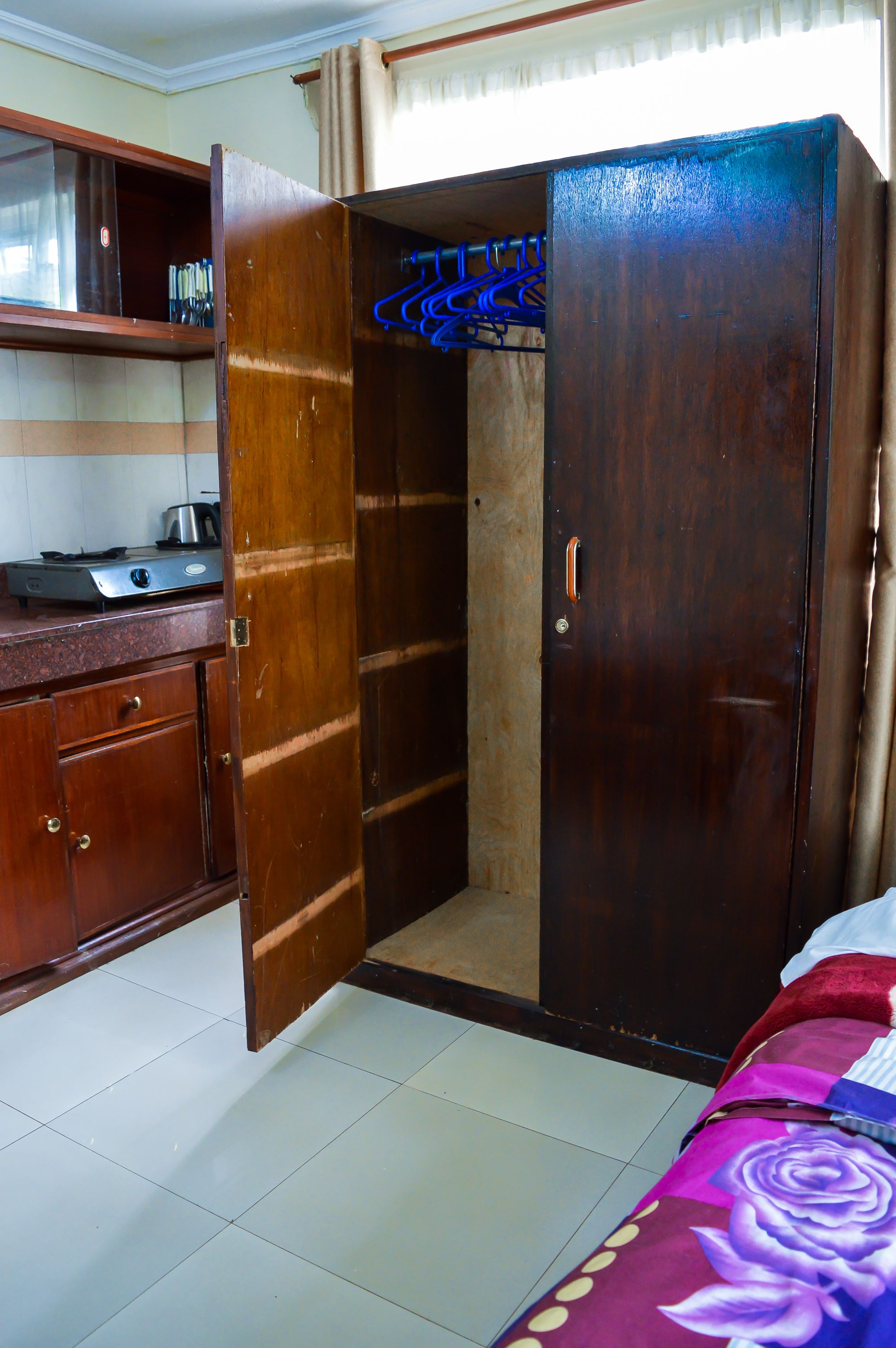 Une pièce avec une armoire en bois, un coin cuisine équipé d’une cuisinière et un lit recouvert d’une couverture colorée.