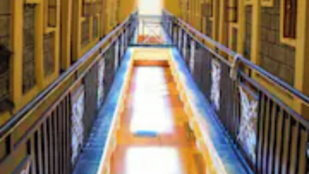 A long, narrow hallway with a central walkway, flanked by doors on both sides, leading to a bright end.