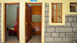 A reception area with a wooden door, a small stool, and a bed with a red blanket.