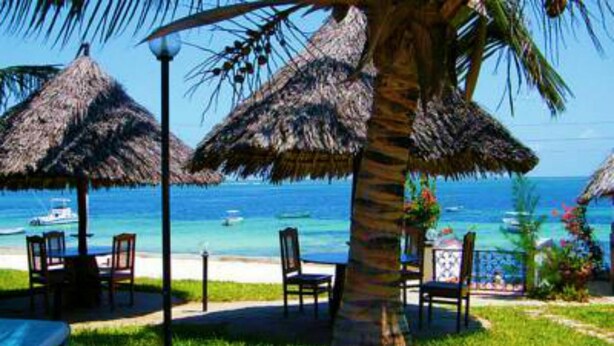 Un espace aménagé avec des sièges, des parasols en chaume et des chaises, le tout situé en bord de plage et offrant une vue sur l’océan.