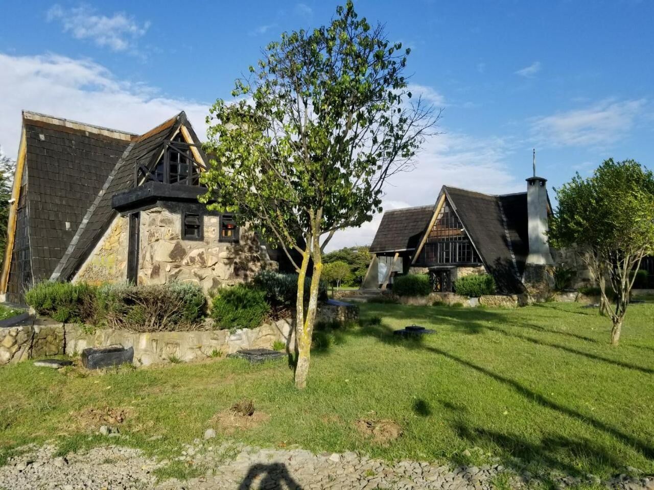A stone building with a sloped roof and a chimney, surrounded by a grassy area and trees.