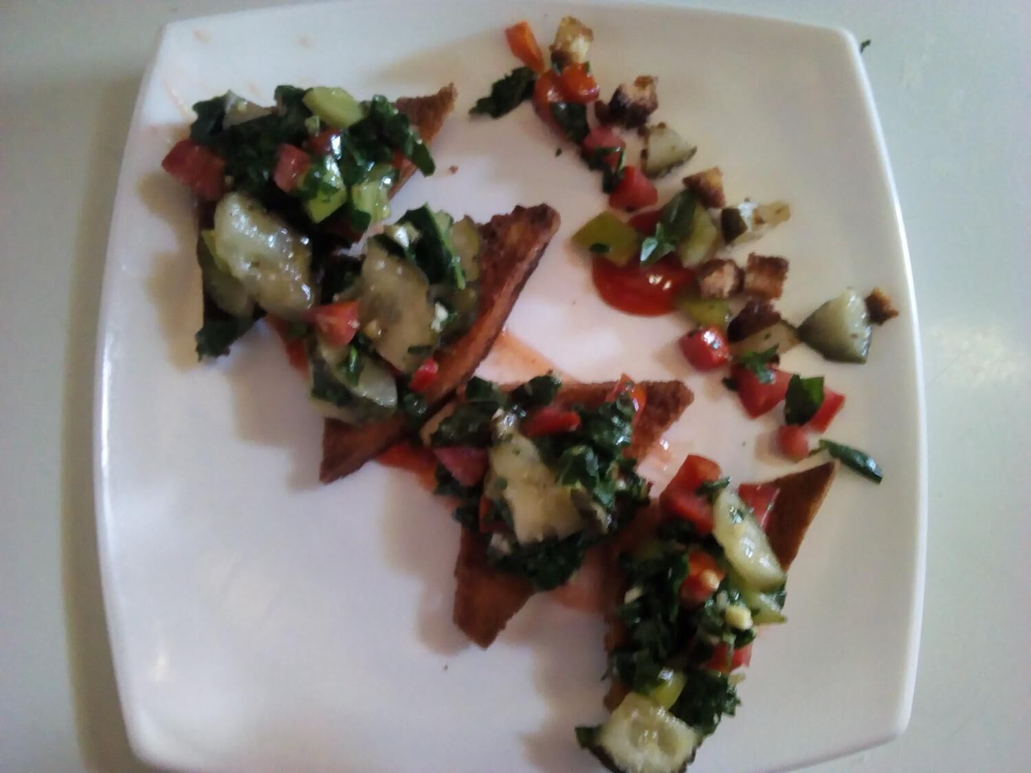 Une assiette blanche contenant un plat composé de pain, de légumes et de fromage.