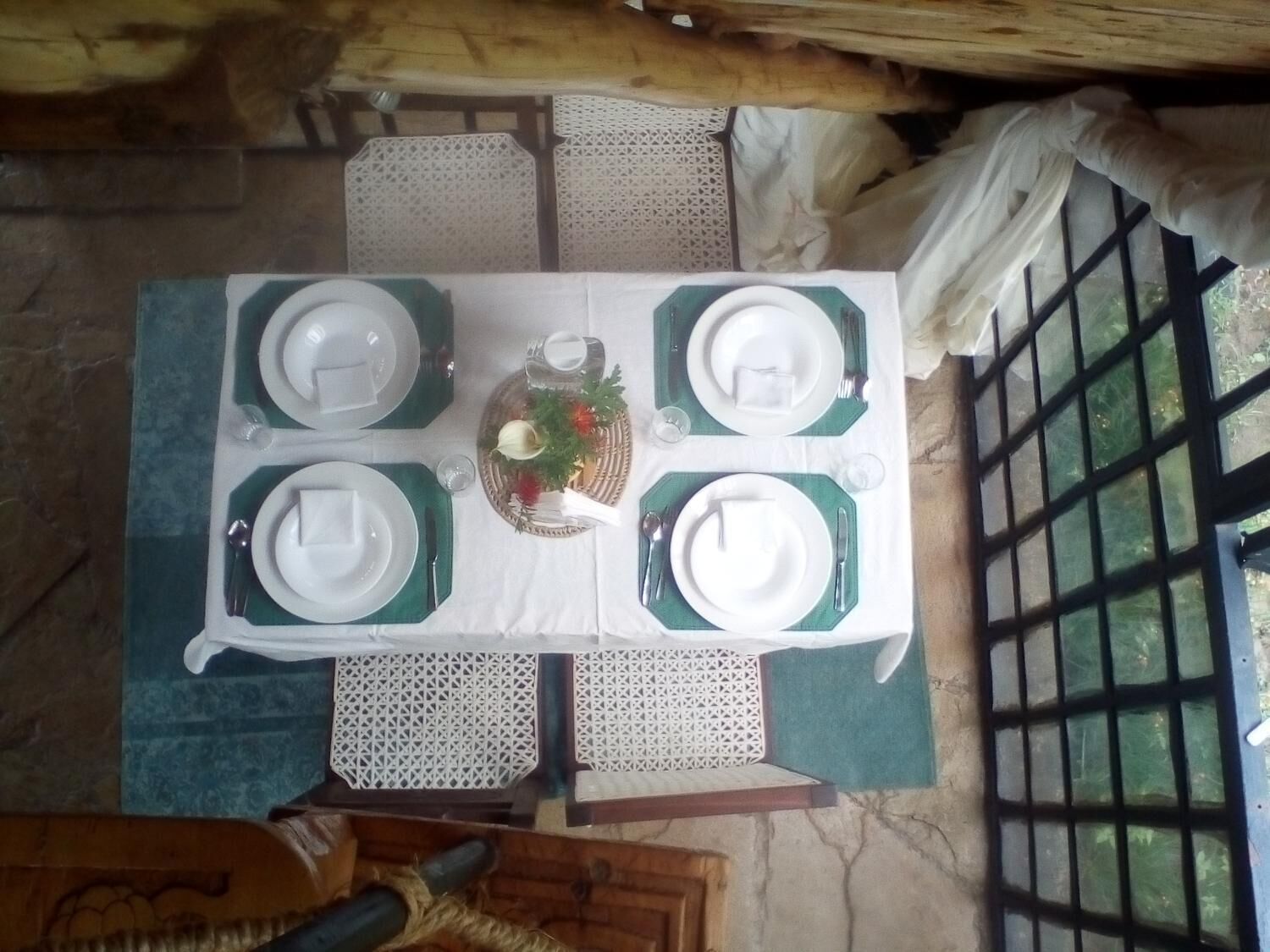 Mesa de comedor preparada para cuatro personas, con platos blancos y servilletas verdes, rodeada de sillas blancas.