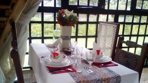 Mesa posta para refeição com toalha branca, jogo americano estampado e um vaso com flores.