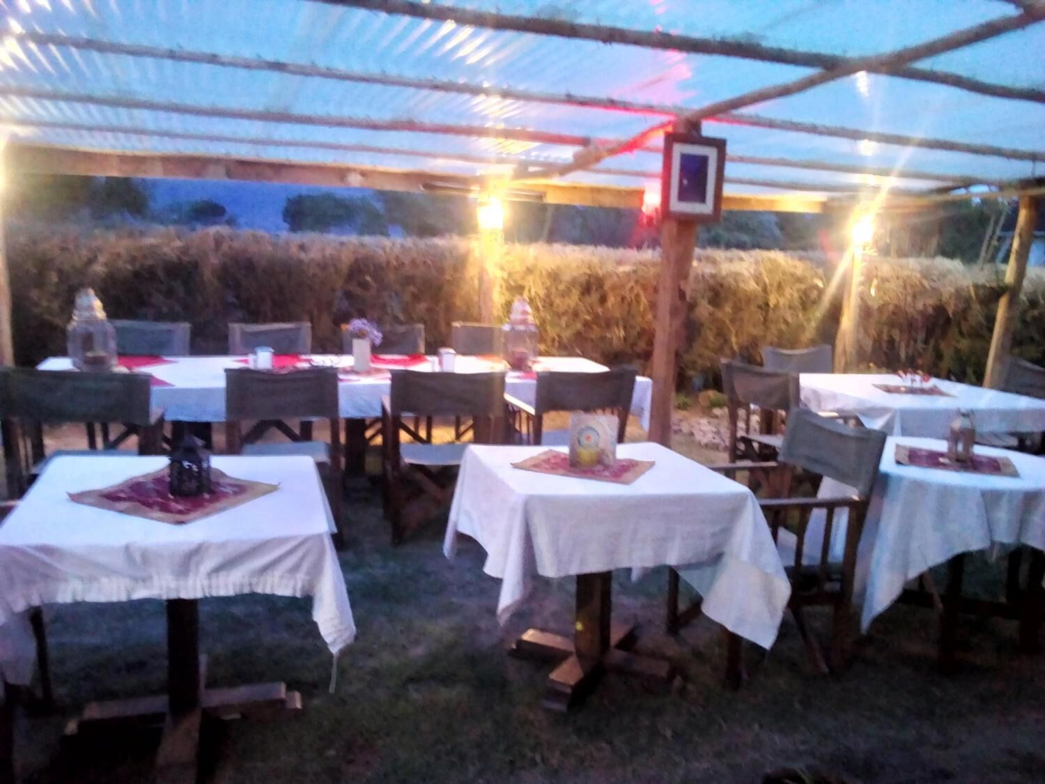 An outdoor dining area with tables and chairs under a covered structure.