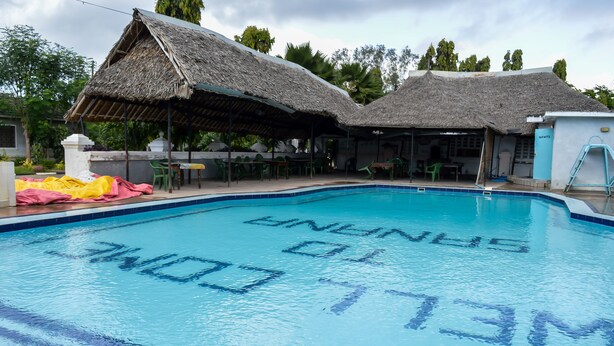 A swimming pool with 'SINGAPORE' written on the water, surrounded by thatched-roof structures and outdoor seating. - Sanana Conference Center and Holiday Resort (Mombasa)