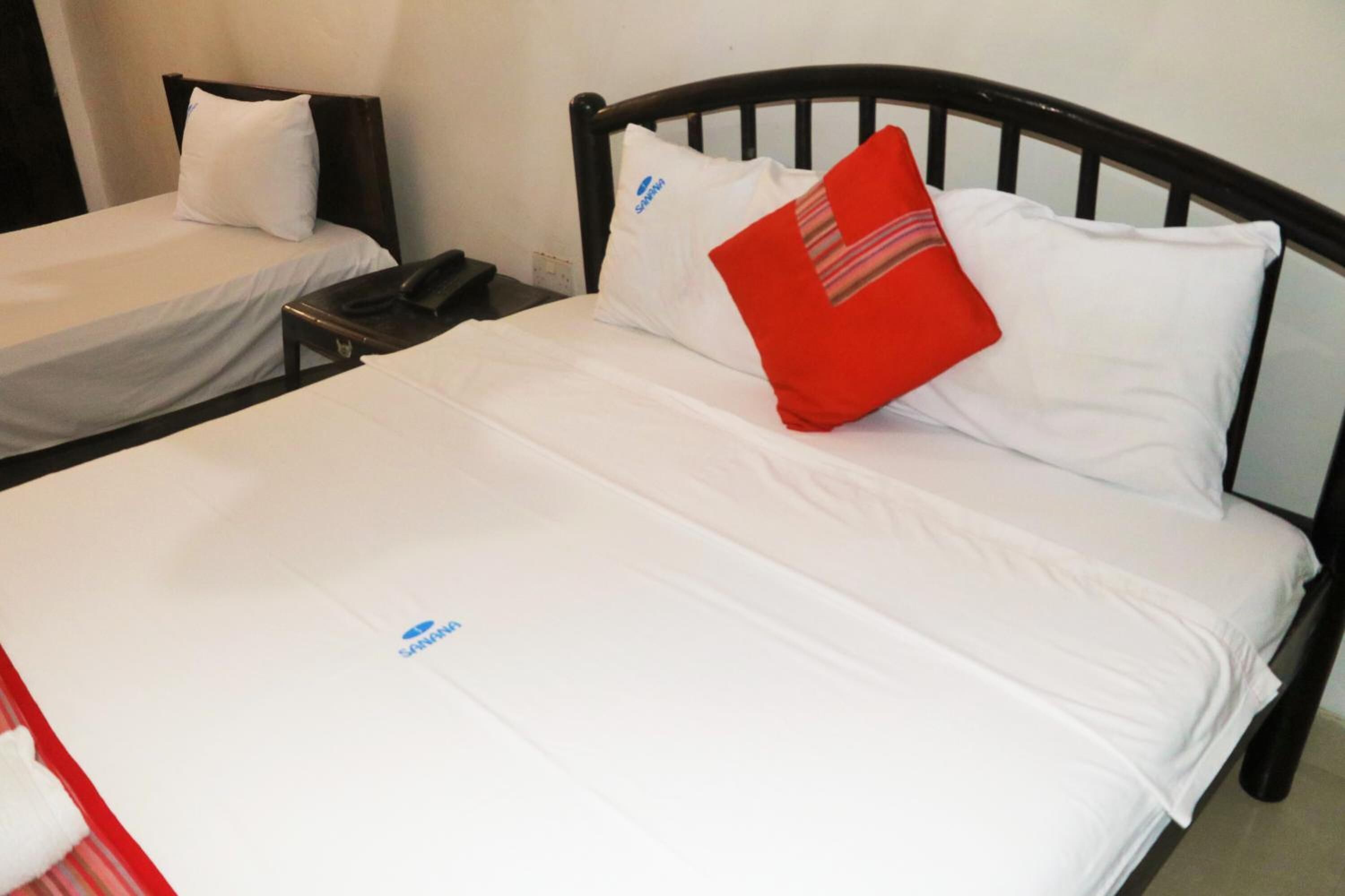 Ein Einzelbett mit weißer Bettwäsche und einem roten Kopfkissen, ein Nachttisch mit Telefon sowie ein wandmontierter Beistelltisch.