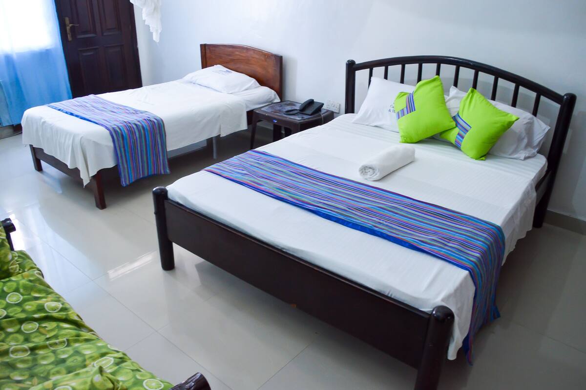 Une chambre d’hôtel avec deux lits simples, un grand lit et une table de chevet avec un téléphone.
