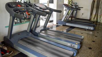 Three treadmills in a gym with a tiled floor and a mirror on the wall.
