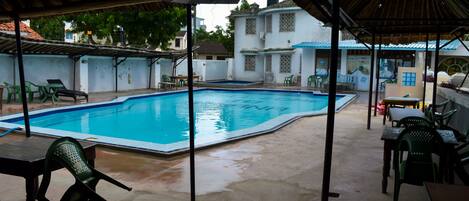 A covered outdoor swimming pool area with chairs and tables, surrounded by buildings.