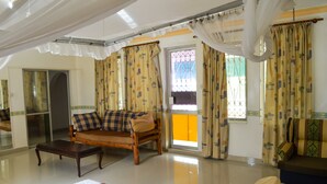 A hotel room with a bed, a sofa, a wooden coffee table, and a balcony with curtains. - Sanana Conference Center and Holiday Resort (Mombasa)