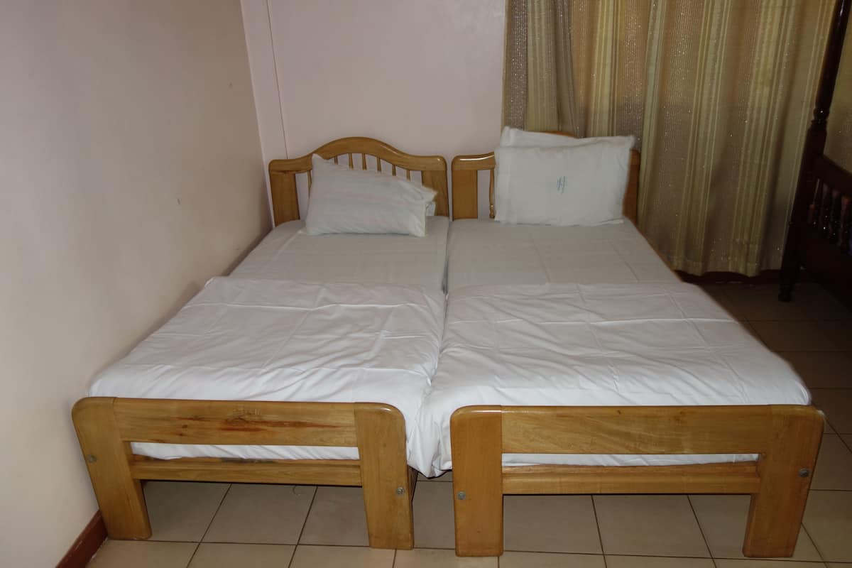 A double bed with wooden headboards and white bedding in a room with tiled flooring.