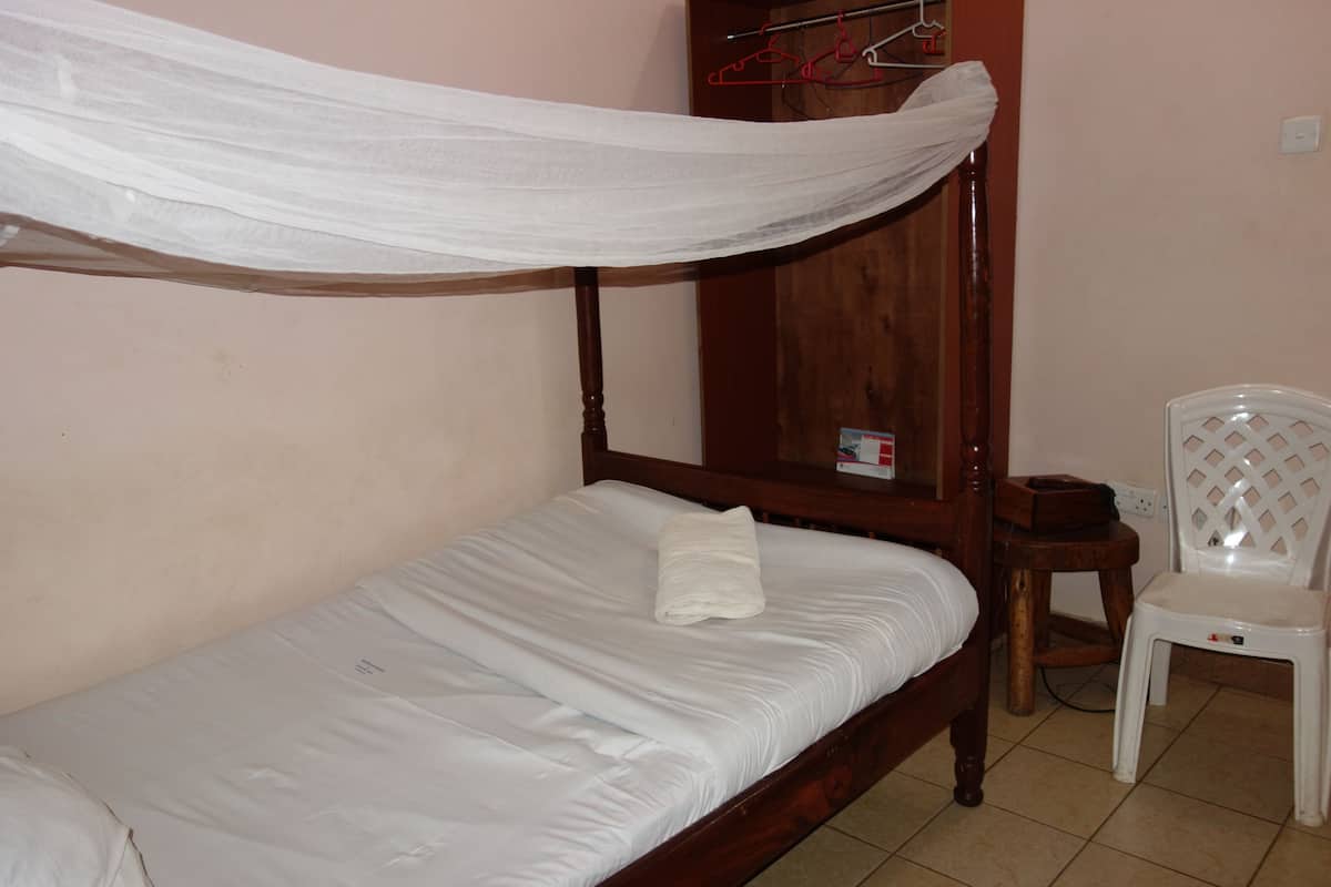 A single bed with a wooden frame and white bedding, a white plastic chair, and a wooden wardrobe with a mirror.
