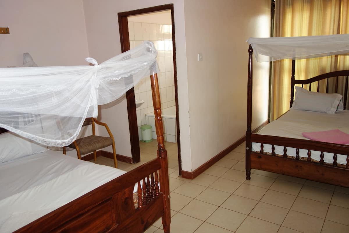 A room with two wooden beds, one with a canopy and one without, a chair, and a tiled floor.